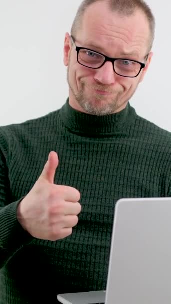 adult man in glasses with a beard mustache is very happy he shows a thumbs up in his hands he has a gray laptop  - Footage, Video