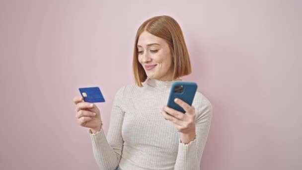 fiatal szőke nő vásárlás okostelefonnal és hitelkártyával izolált rózsaszín háttér - Felvétel, videó