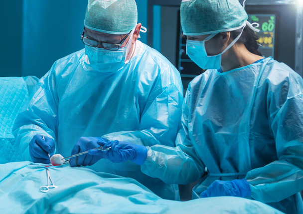 Diverse team of professional medical doctors performs a surgical operation in a modern operating room using high-tech equipment and technology. Surgeons are working to save the patient in the hospital - Foto, imagen
