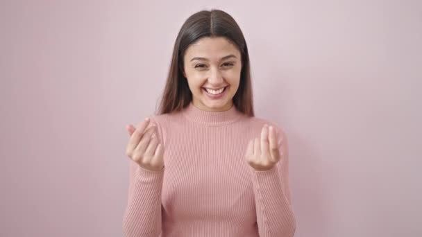 Giovane bella donna ispanica sorridente fiducioso facendo spendere soldi gesto su isolato sfondo rosa - Filmati, video