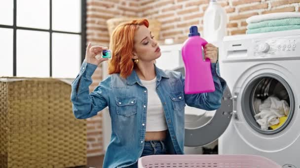 Nuori punapää nainen pesee vaatteita valitsemalla pesuaine pesutuvassa - Materiaali, video