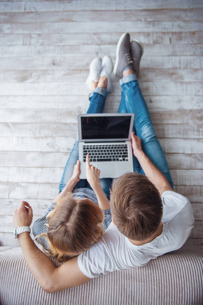 Felülnézet a szép fiatal pár alkalmi ruhát használ egy laptop ülve a padlón ellen, szürke fal - Fotó, kép