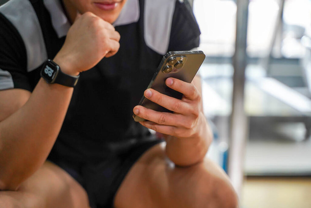 Fechar e cortar asiático cara relaxante de treino com telefone móvel no centro de fitness. - Foto, Imagem