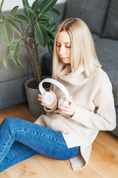 Jonge blonde vrouw in koptelefoon luisteren naar muziek en ontspannen thuis. - Foto, afbeelding