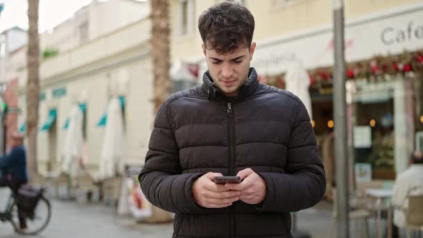 Jonge Spaanse man met smartphone die wegkijkt op het terras van de coffeeshop - Video