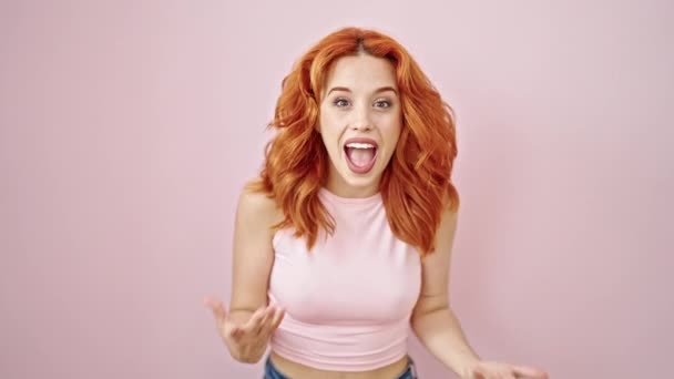 Νεαρή κοκκινομάλλα γυναίκα δείχνει τον εαυτό της με έκφραση έκπληξη πάνω από απομονωμένο ροζ φόντο - Πλάνα, βίντεο