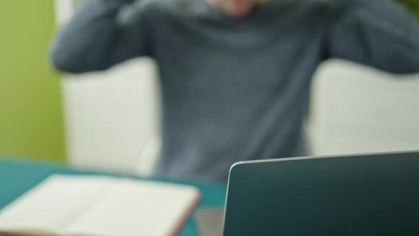 Joven hispano usando laptop sentado en la mesa usando auriculares en el comedor - Imágenes, Vídeo