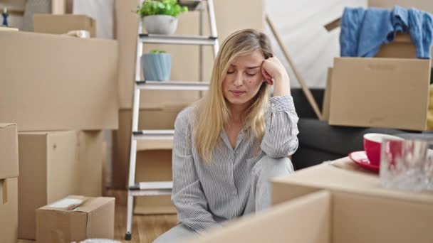 Nuori blondi nainen istuu lattialla stressaantunut ilme uudessa kodissa - Materiaali, video