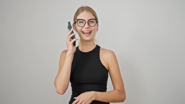 Nuori blondi nainen puhuu älypuhelimella hymyillen eristetyllä valkoisella taustalla - Materiaali, video