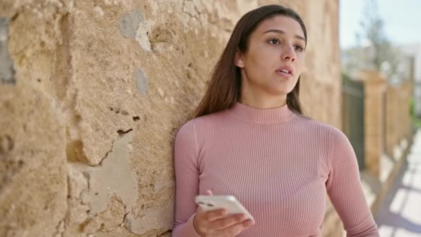 Jonge mooie Spaanse vrouw met behulp van smartphone met serieuze expressie op straat - Video