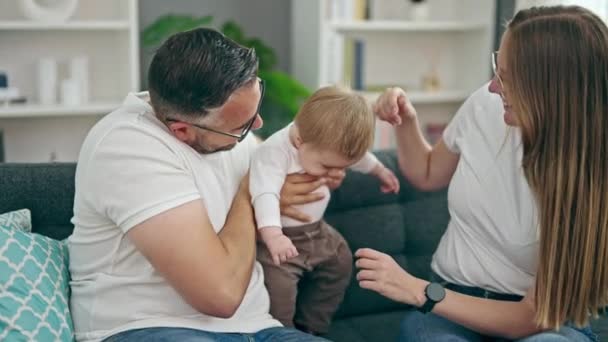 Familia de madre, padre y bebé sonriendo sentados en el sofá en casa - Imágenes, Vídeo