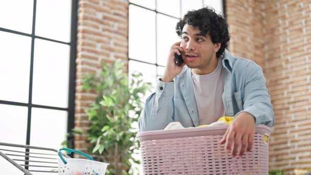 Молодий латинський чоловік розмовляє на смартфоні, вішаючи одяг на лінії одягу в пральні
 - Кадри, відео