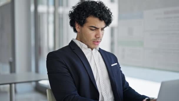 Mladý latinsky muž obchodní pracovník pomocí notebooku vypadající rozrušený v kanceláři - Záběry, video
