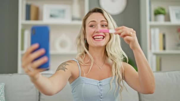 Mladá blondýna žena s video hovor držení těhotenský test usměvavý doma - Záběry, video