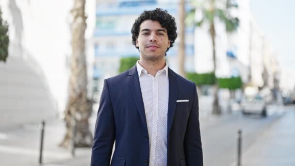 Giovane latino uomo d'affari lavoratore sorridente fiducioso che punta alla fotocamera in strada - Filmati, video