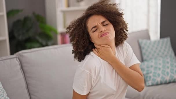 Joven mujer hispana hermosa sentada en el sofá sufriendo por el dolor cervical en casa - Imágenes, Vídeo
