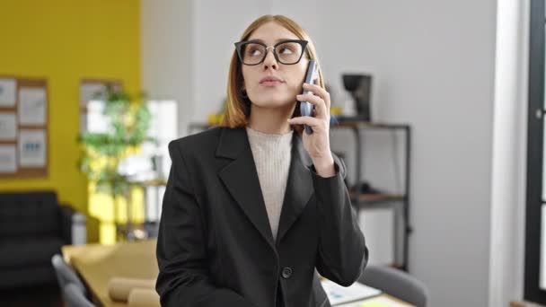 Молодая блондинка бизнес-работница разговаривает на смартфоне, работая в офисе - Кадры, видео