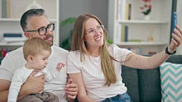 Familia de madre, padre y bebé tomando selfie sentado en el sofá en casa - Metraje, vídeo