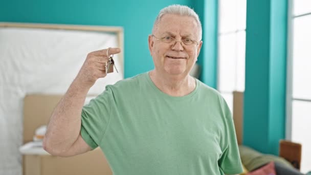 Grauhaariger Mann mittleren Alters lächelt zuversichtlich und hält Schlüssel im neuen Zuhause - Filmmaterial, Video