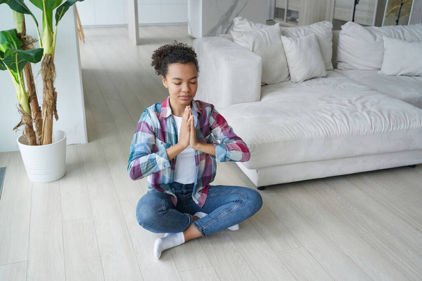 Calma biracial ragazza pratica yoga in posa loto a casa, promuovendo stile di vita sano e sollievo dallo stress. - Foto, immagini