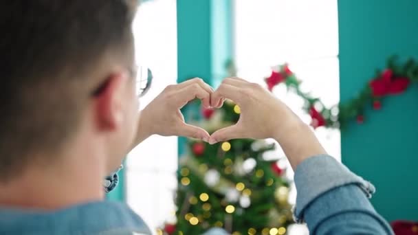 Νεαρός Ισπανός που κάνει σχήμα καρδιάς με τα χέρια του να γιορτάζουν τα Χριστούγεννα στο σπίτι - Πλάνα, βίντεο