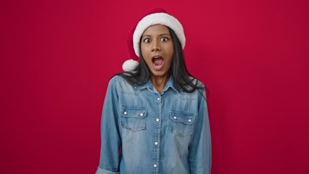 Afrikai amerikai nő meglepetés kifejezés visel karácsonyi kalap felett elszigetelt piros háttér - Felvétel, videó