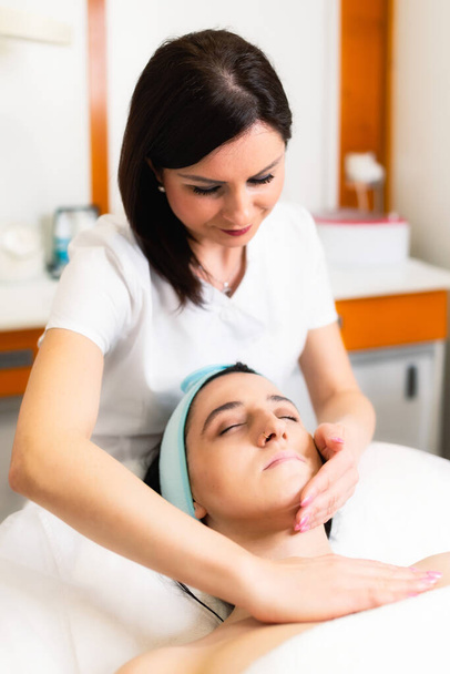 esteticista haciendo masaje facial a una joven beata. - Foto, imagen
