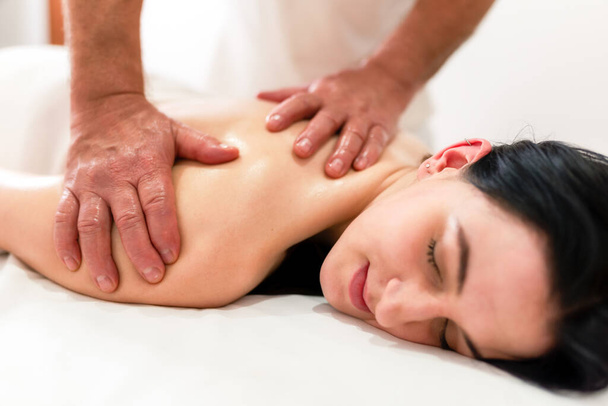 Die Hände des Chiropraktikers oder Masseurs machen eine entspannende Rücken- und Armmassage für die liegende Frau auf dem Tisch. Professionelle Mann Arzt Masseur während der Arbeit mit Patienten. - Foto, Bild