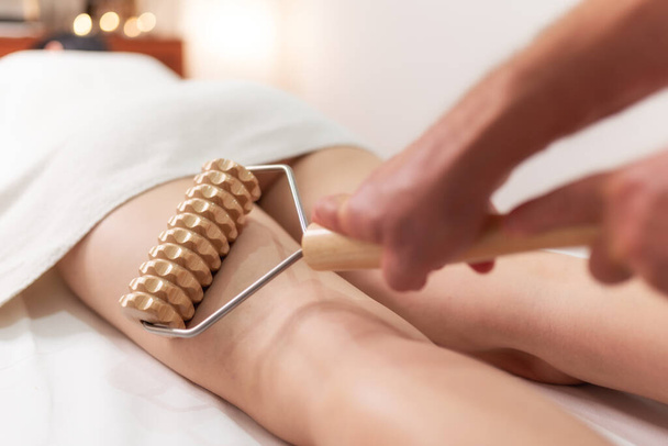 Stimulation of the lymphatic system with wood therapy body treatment. Massage of legs with wooden roller to eliminate liquids and cellulite. Improve circulation in the legs - Photo, Image
