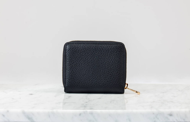 Luxus női táska, pénztárca. Luxus fekete bőrtáska fehér háttérrel, márvány padlón. A kamera a pénztárca előtt van. Divatos trendi kiegészítő - Fotó, kép
