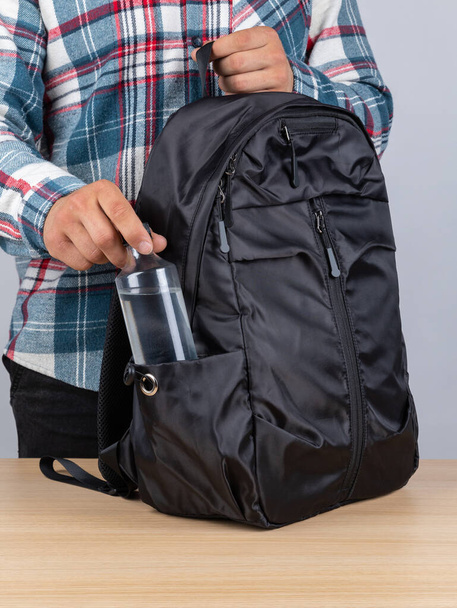 Κοντινό πλάνο ενός νεαρού φοιτητή που βγάζει ένα μπουκάλι νερό από το σακίδιό του.. - Φωτογραφία, εικόνα