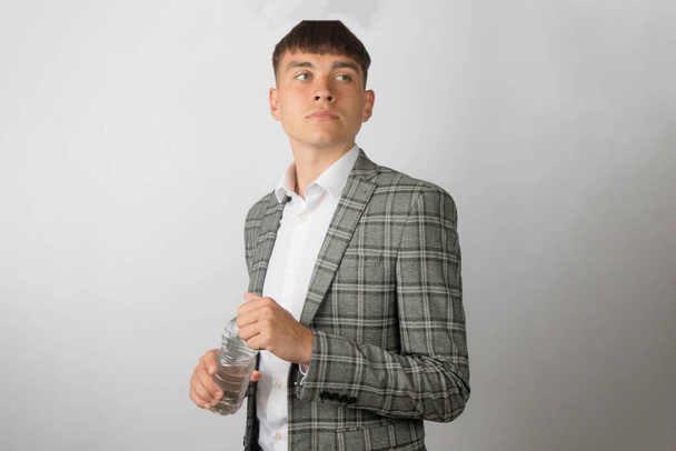 Young entrepreneur wearing a suit jacket and open neck shirt without a tie opeing a plastic bottle of water - Фото, зображення