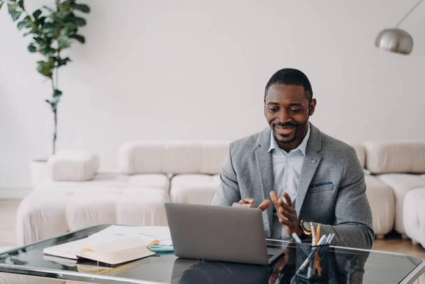 Αφροαμερικανός επιχειρηματίας σε βιντεοκλήση, συζητώντας με συνάδελφο, χρησιμοποιώντας φορητό υπολογιστή στο γραφείο. - Φωτογραφία, εικόνα