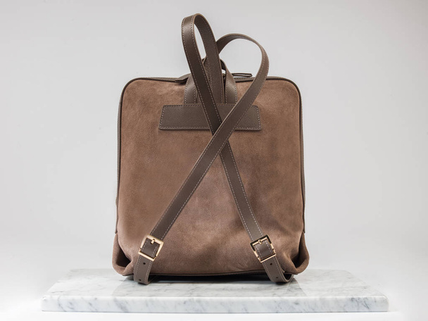 Luxury suet backbag, unisex backbag. Luxury, brown leather and suet backbag on white background, on marble floor. A elegant bag is see from back side. Fashionable trendy. - Foto, imagen