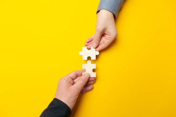 Dos manos conectan rompecabezas sobre un fondo amarillo. Cooperación y trabajo en equipo en los negocios. Colaboración personas para el éxito. - Foto, imagen