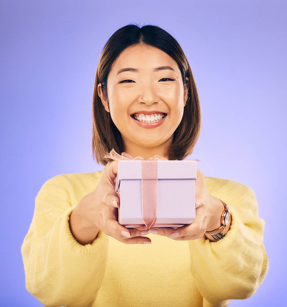 Portrait, smile and Asian woman with a gift, box and celebration against a studio background. Face, happy female person or model with happiness, present and giveaway with a ribbon, surprise and prize. - Foto, Imagen