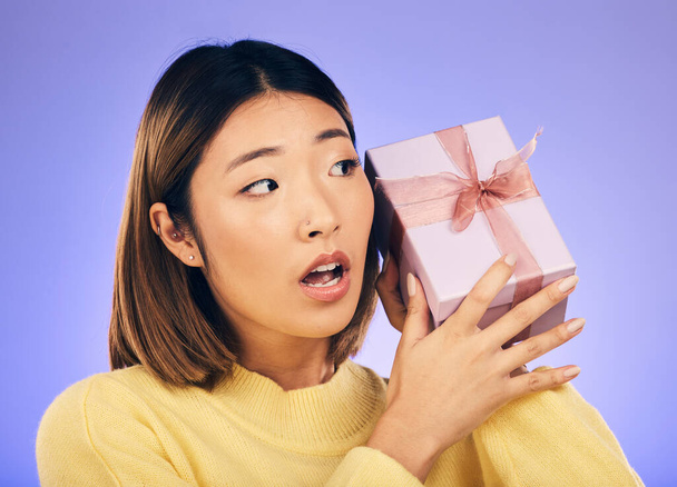 Thinking, gift and box with face of asian woman in studio for birthday, celebration and curious. Surprise, wow and party with female person and present on purple background for giveaway and package. - Fotografie, Obrázek