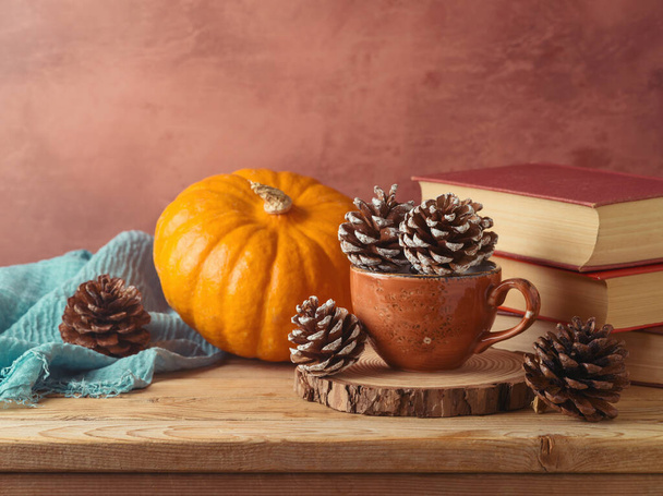 Autumn concept with pine cone in coffee cup, pumpkin and books on wooden table. Thanksgiving greeting card - Foto, Imagem