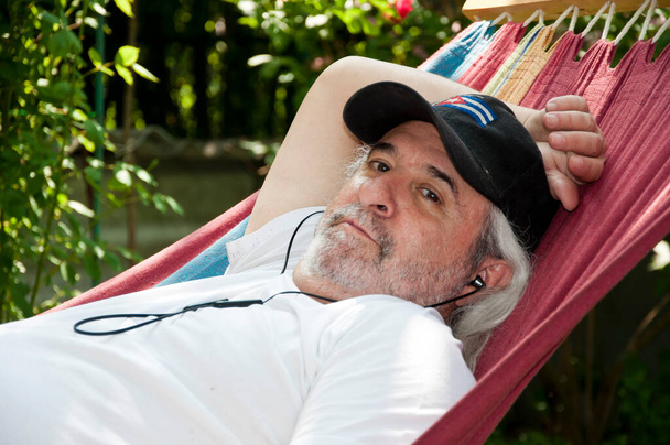summer vacation. Leisurely retreat for the old man in his hammock. Relaxed old man lounging in a hammock. Tranquil moments for the old man in the hammock. - Photo, Image