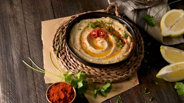 Delicious hummus in ceramic bowl. Colorful snack composition on a black wooden background. - Фото, зображення