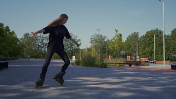sportos lány lovagol görkorcsolya a parkban a város hátterében Aktív lány élvezi görkorcsolyázás lecke utca utca sport koncepció - Felvétel, videó