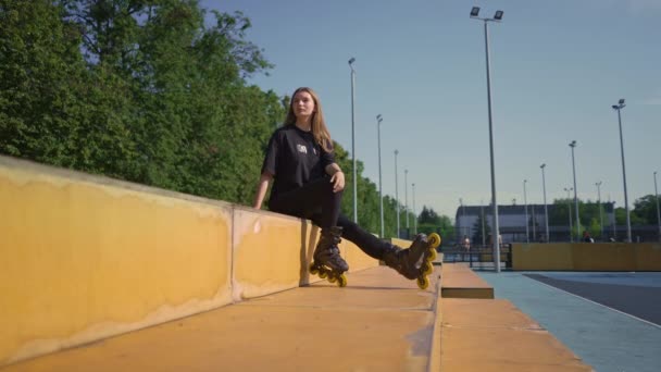 sportief meisje na rolschaatsen rust op het sportveld bedachtzaam blij met de straat sport les - Video
