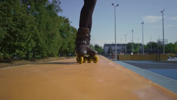 chica deportiva practicando trucos en patines en el fondo del parque de la ciudad disfrutando de la lección de patinaje sobre ruedas de cerca piernas street sport - Imágenes, Vídeo