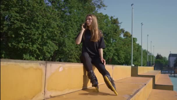 sport meisje na rolschaatsen rust op het sportveld praten op telefoon straat sport actieve levensstijl - Video