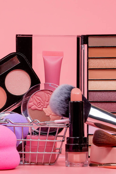 Various make-up products and brushes in shopping cart on pink background. Makeup cosmetics sale concept. - Photo, Image