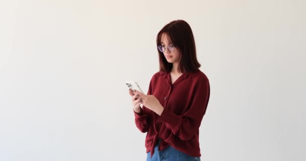 Caucasian teenage girl as she navigates through a white background while using her phone. In a state of stress and anxiety, she frantically attempts to undo a certain action on her device. - Footage, Video