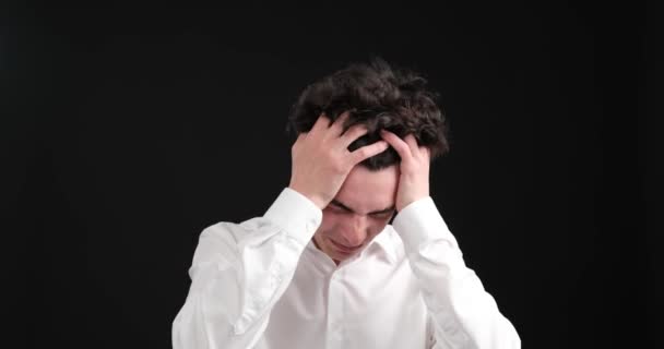 Caucasian man on a black background, experiencing the discomfort of a severe headache. With a pained expression on his face, he clutches his head, indicating the intensity of the pain he is enduring. - Footage, Video
