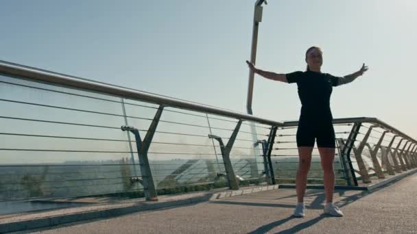Γυμναστική νεαρή αθλήτρια κορίτσι το πρωί κάνει προθέρμανση ασκήσεις πριν από την κατάρτιση στο δρόμο στην πόλη στη γέφυρα Αθλητισμός υγεία - Πλάνα, βίντεο
