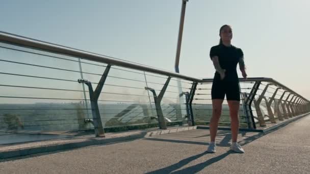 Γυμναστική νεαρή αθλήτρια κορίτσι το πρωί κάνει προθέρμανση ασκήσεις πριν από την κατάρτιση στο δρόμο στην πόλη στη γέφυρα Αθλητισμός υγεία - Πλάνα, βίντεο
