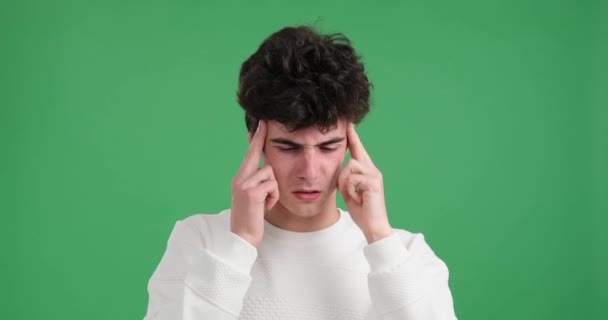 Blanke man lijdt zichtbaar aan een ernstige hoofdpijn tegen een boeiende groene achtergrond. Met een pijnlijke uitdrukking en een hand rustend op zijn tempel, brengt hij de intensiteit van zijn hoofdpijn over. - Video